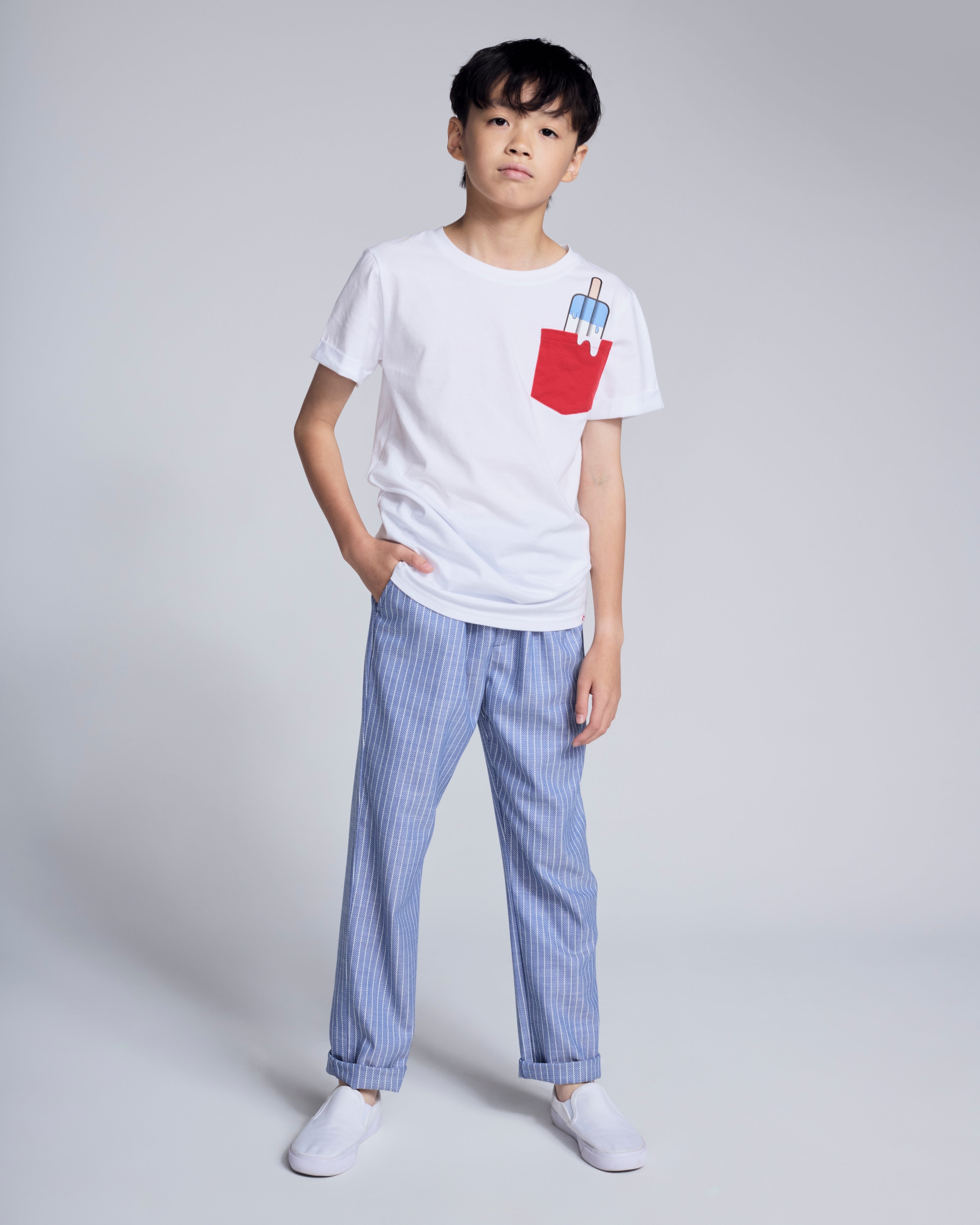 Boy wearing Popsicle White Day Trip Tee with a playful popsicle pocket and striped pants.