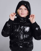 Girl wearing a Glitter Black Slim Puffy Coat with a shiny black finish and hood.