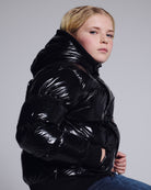 Glitter Black Slim Puffy Coat worn by a young girl, showcasing its shiny black design and cozy fit for stylish warmth.