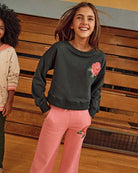 A smiling girl wearing the Rose Sweat Set featuring a rose design on the shirt and pants.