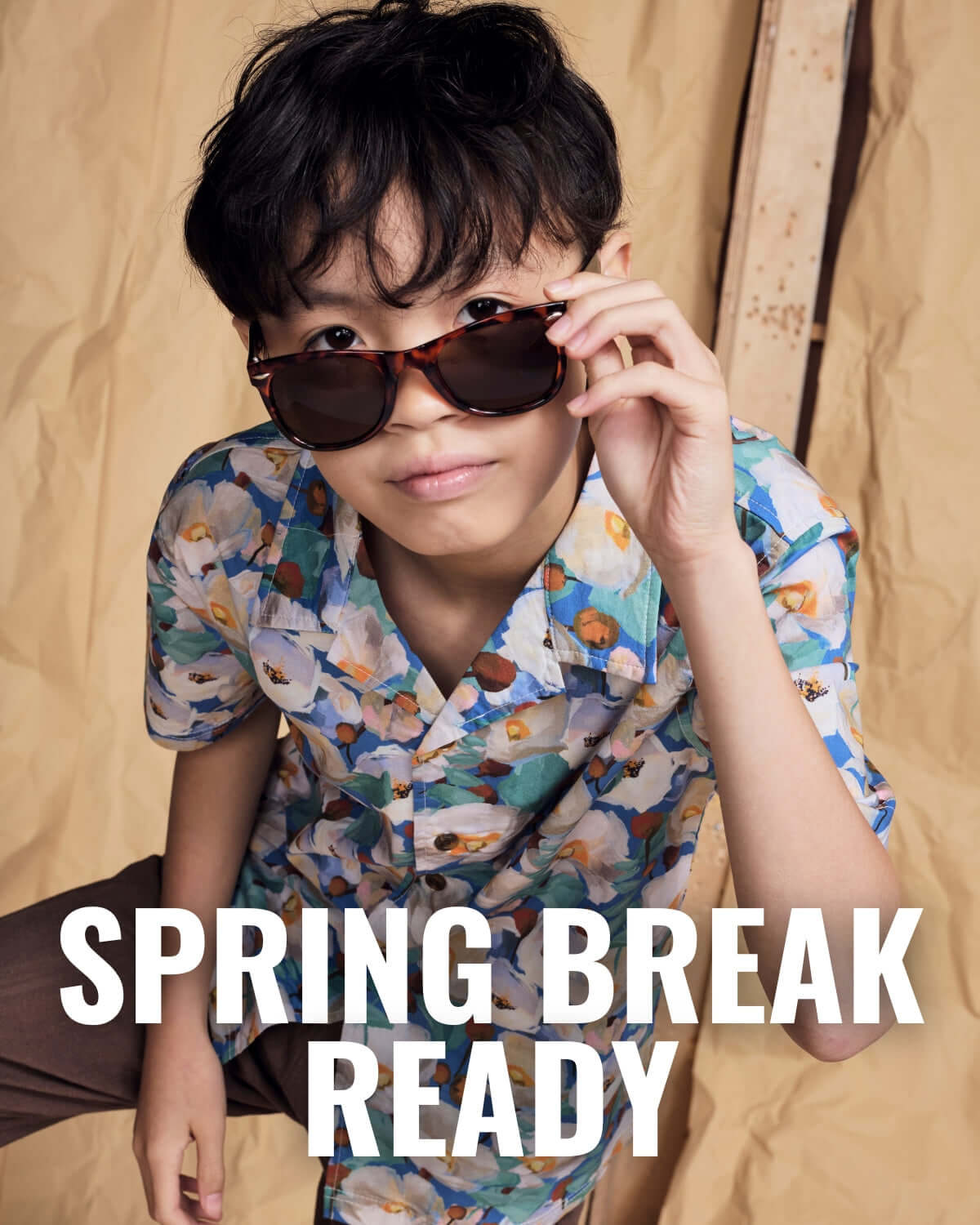 Child wearing sunglasses and blue casual button up with 'Spring Break Ready' text on a beige background