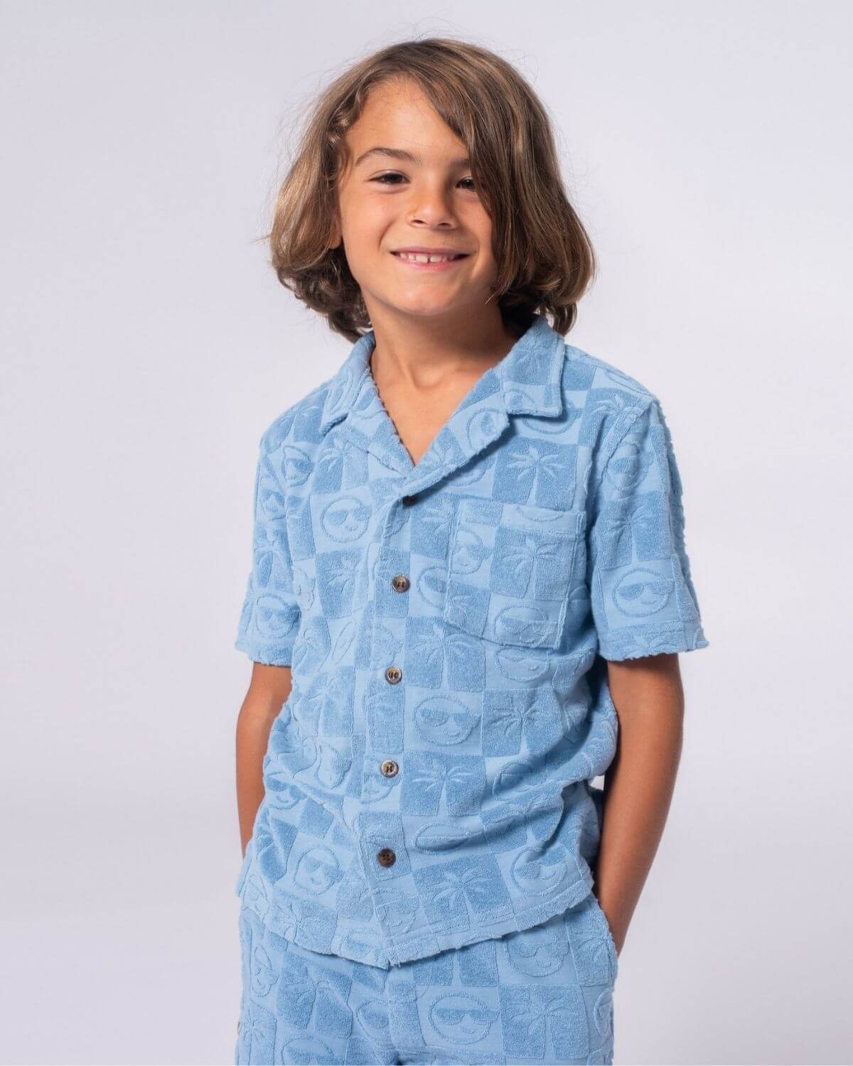 Blue Resort Terry Shirt on a smiling boy, featuring palm trees and sunglasses designs, perfect for summer adventures.