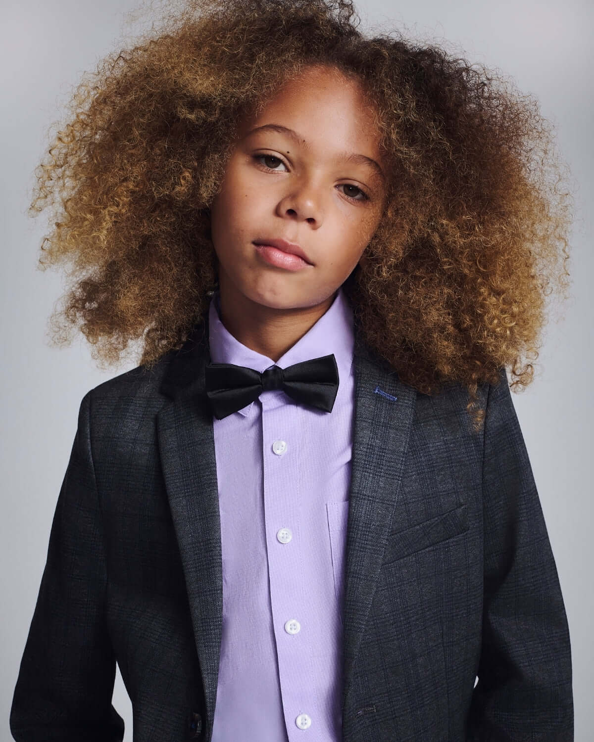 Child wearing a black silk bow tie with a stylish blazer and purple shirt, showcasing sophistication.