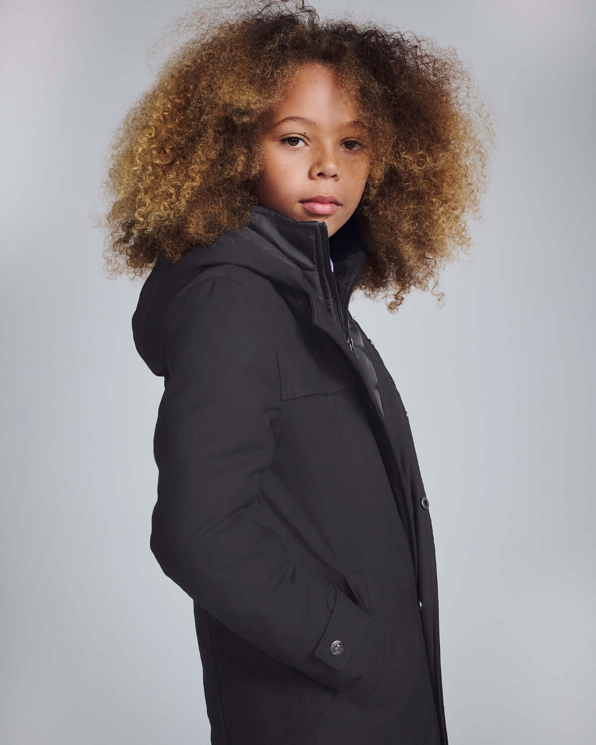 Black Urban Gotham Coat worn by a child with curly hair, showcasing its stylish and sleek design.