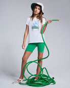 Girl wearing Tropical Green Biker Short and t-shirt, holding a garden hose.