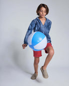 Child wearing a Waterfall Terry Baja Pullover, playing with a beach ball and wearing red shorts.