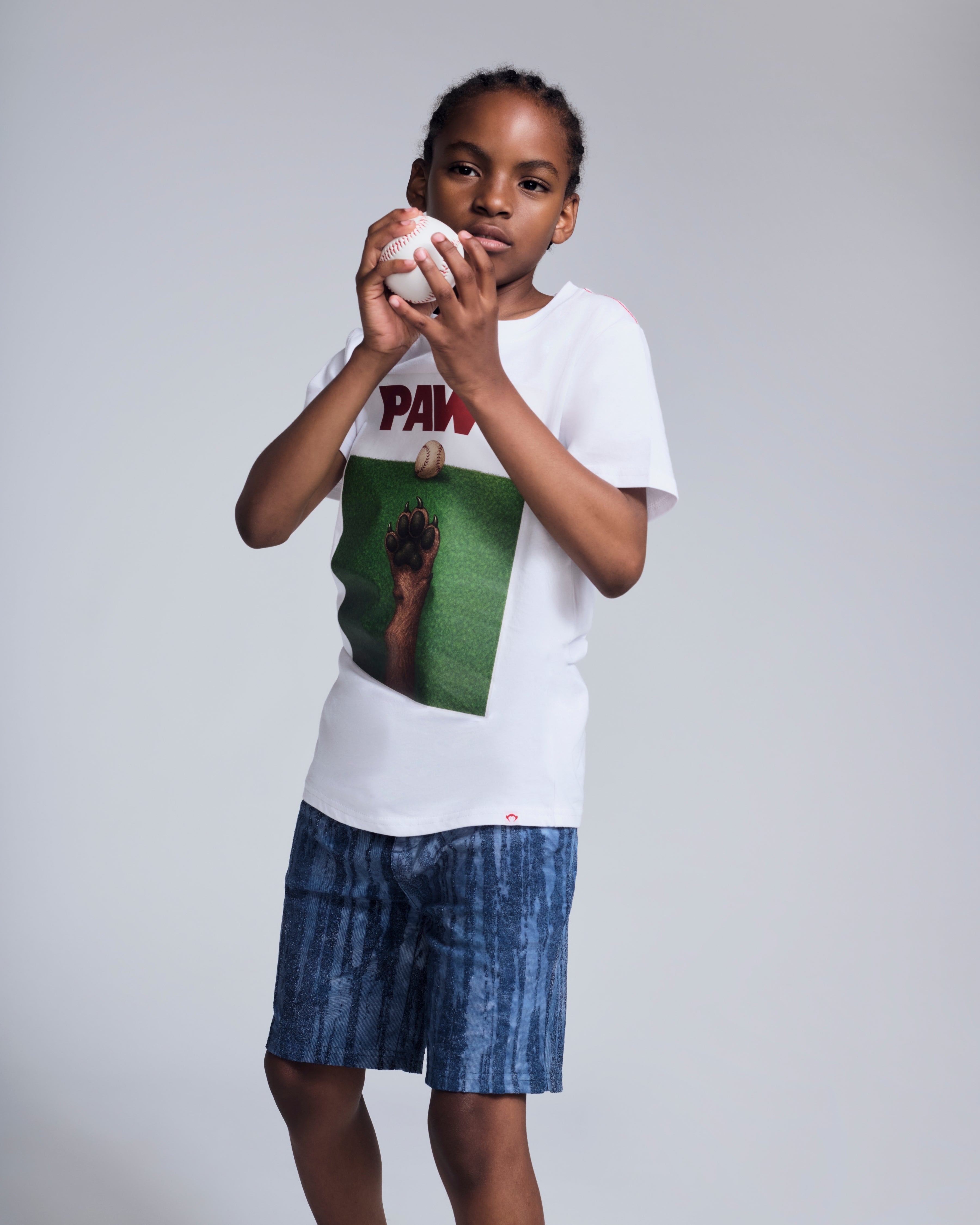 Child wearing a graphic tee and Waterfall Preston Short, ready to play with a baseball.