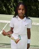 Girl in a white tennis outfit holding a trophy on a tennis court