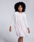 Girl wearing a White Rose Empire Dress with floral print and front bow detail.