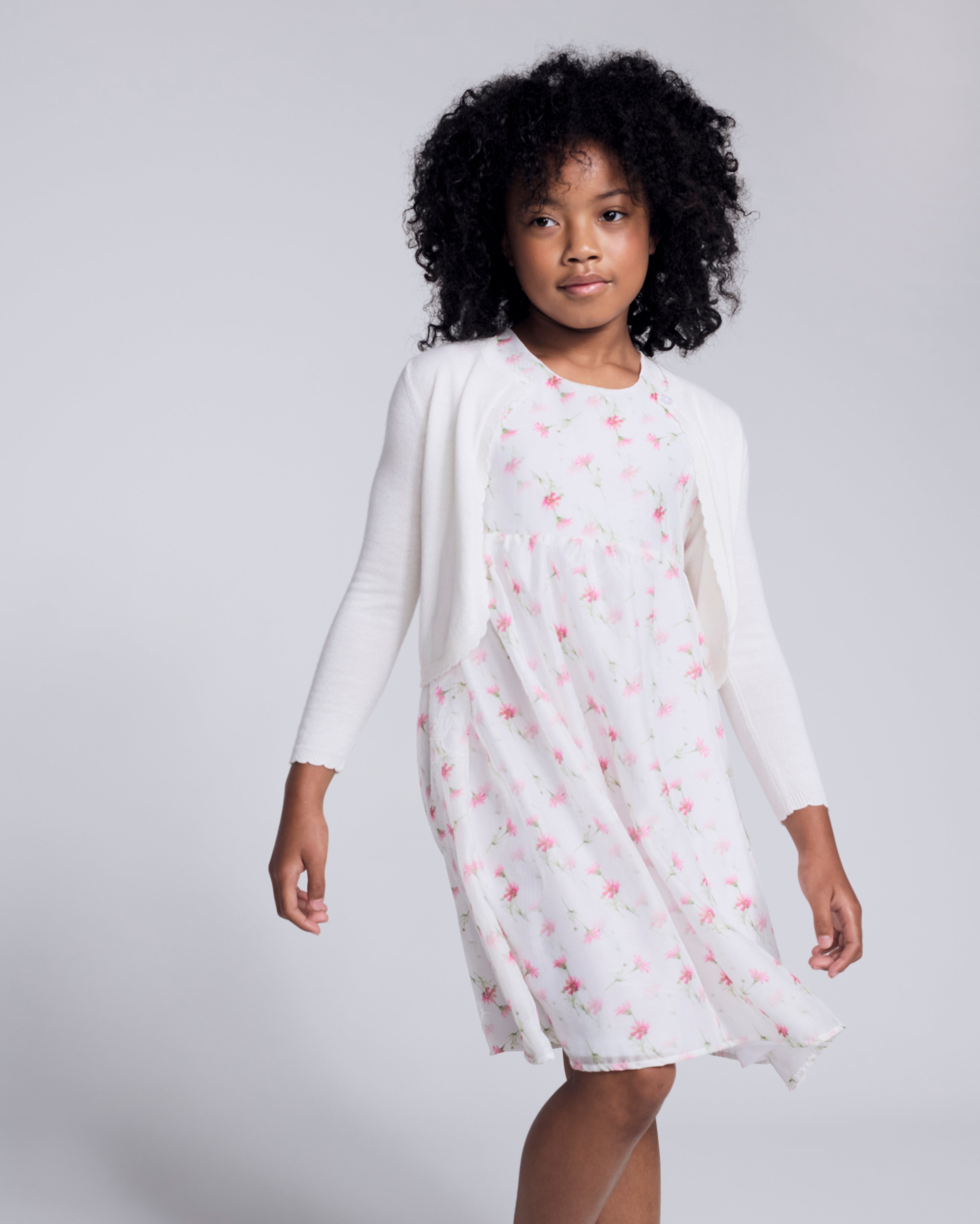 Girl wearing a White Rose Empire Dress with floral print and front bow detail.