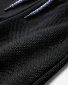 Close-up of a black textured knit fabric with a white and black herringbone patterned drawstring.