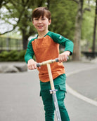 Boy riding a scooter wearing a Terracotta Baseball Tee and green sweatpants outdoors.