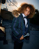 Black Watch Tartan City Transit Coat worn by a child holding a microphone against a sunset backdrop.