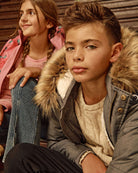 Boy wearing a Grey Denali Down Coat with fur trim and sherpa lining, sitting next to a girl in a pink jacket.