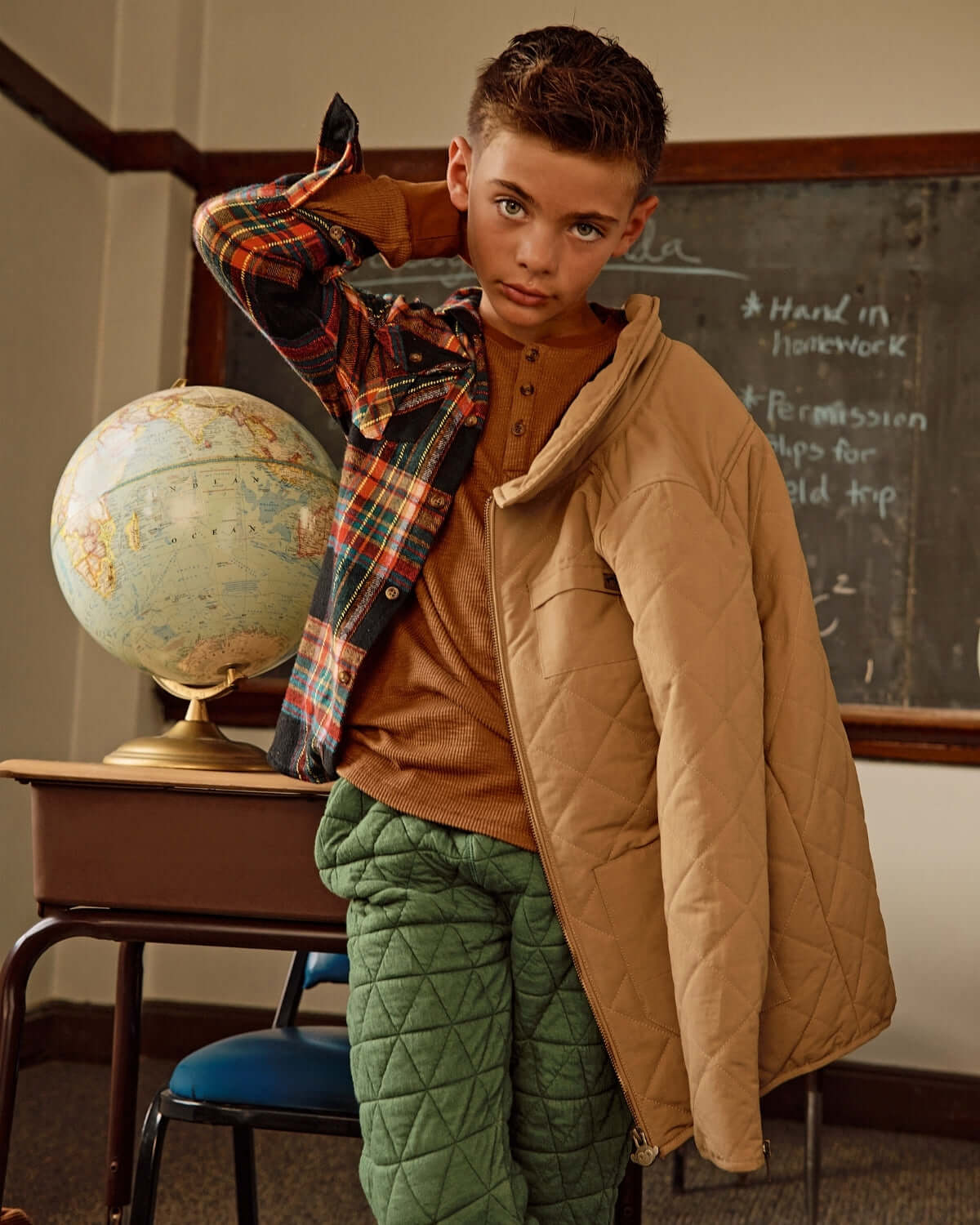 Boy wearing a khaki flight jacket, showcasing a stylish look in a classroom setting with a globe.