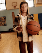Boy wearing Lumber Plaid Glen Flannel Hoodie holding a basketball in a gym setting.