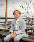Young boy wearing High Rise Grey Stretchy Suit Pants, seated on a boat, styled for a formal occasion.