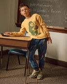 A boy wearing Wilderness Highland Fleece Sweatpants and a yellow sweatshirt, posing in a classroom setting.