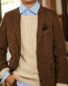 A close-up of a person wearing a brown corduroy blazer over a cream cable-knit sweater, a light blue and white striped dress shirt, and a dark pocket square.