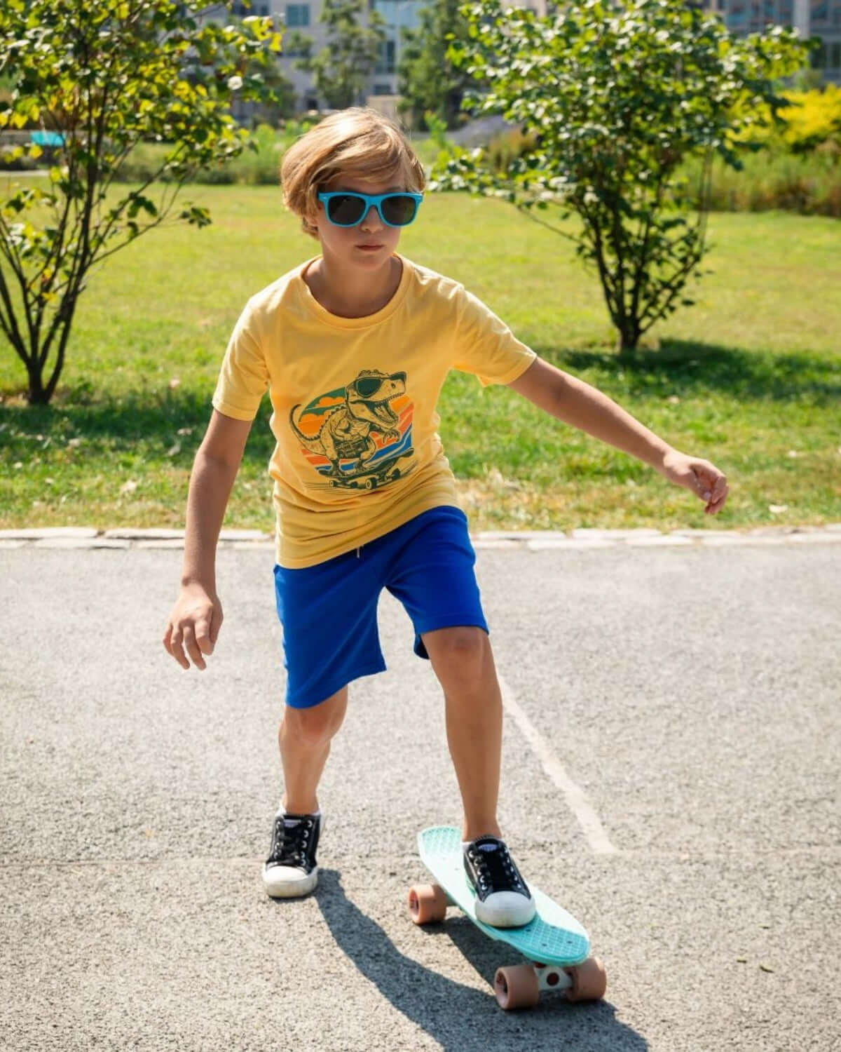 A boy skateboarding in Nautical Blue Preston Shorts and a yellow t-shirt during a sunny day.