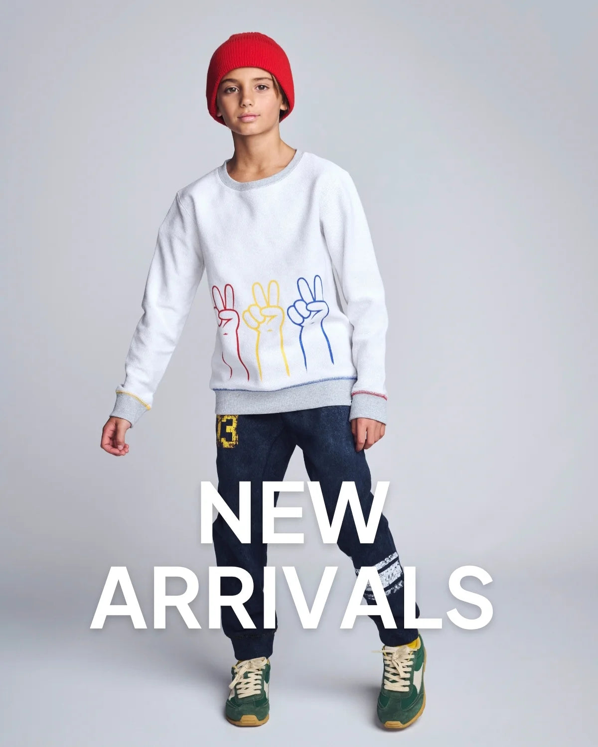 Person wearing a white sweatshirt with colorful designs, dark jeans, and green shoes on a gray background with 'NEW ARRIVALS' text.