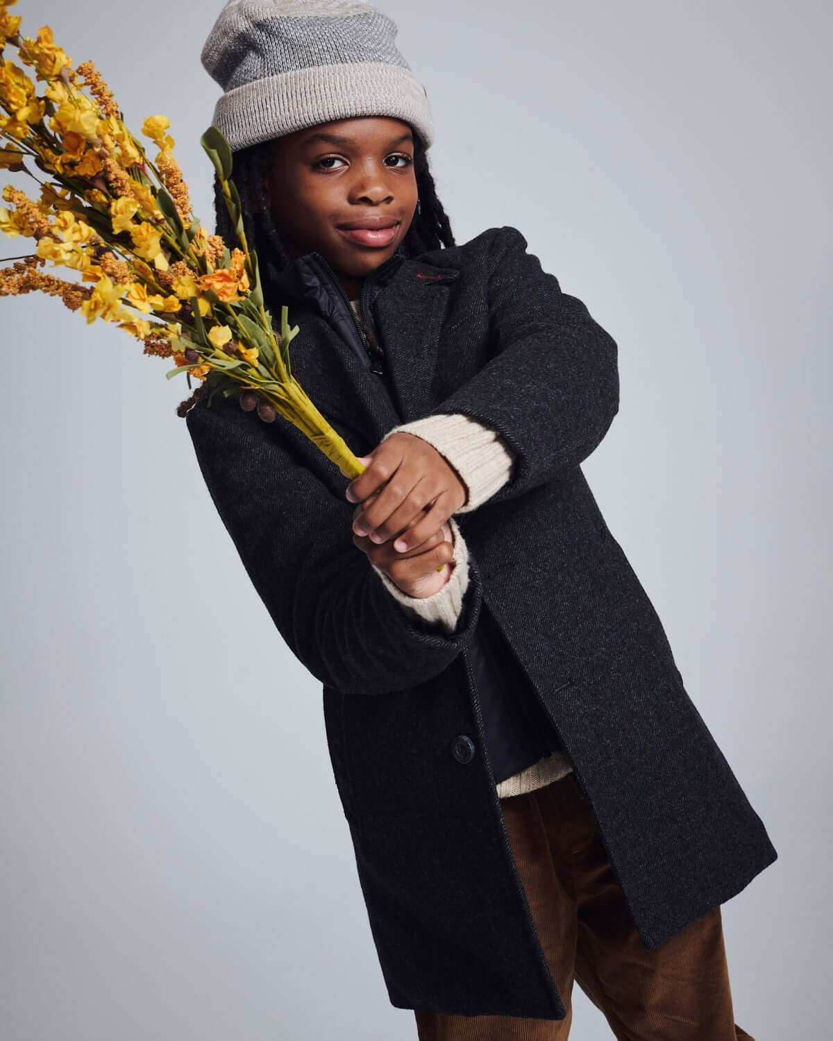 Child wearing a Black Tweed New City Overcoat, holding flowers, styled with a grey hat.
