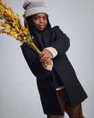 Child wearing a Black Tweed New City Overcoat, holding flowers, styled with a grey hat.
