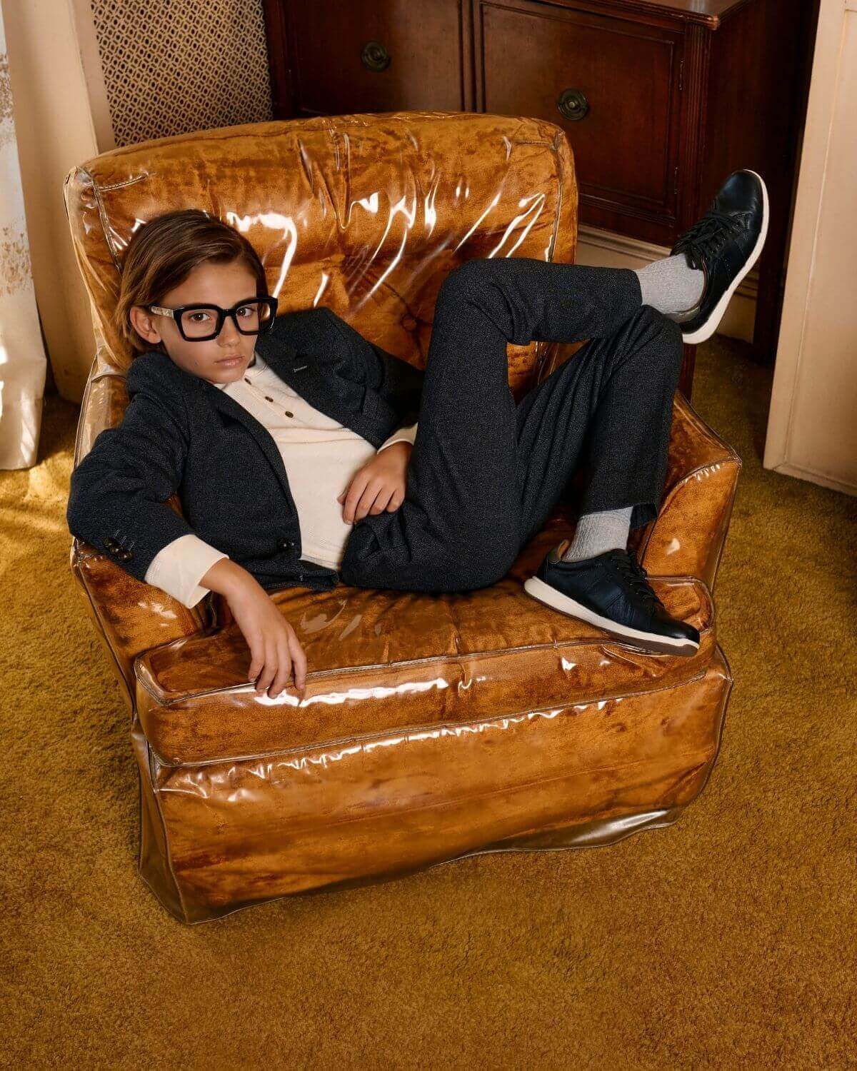 A child lounging in a black herringbone stretchy mod suit on a vintage chair, showcasing comfort and style.