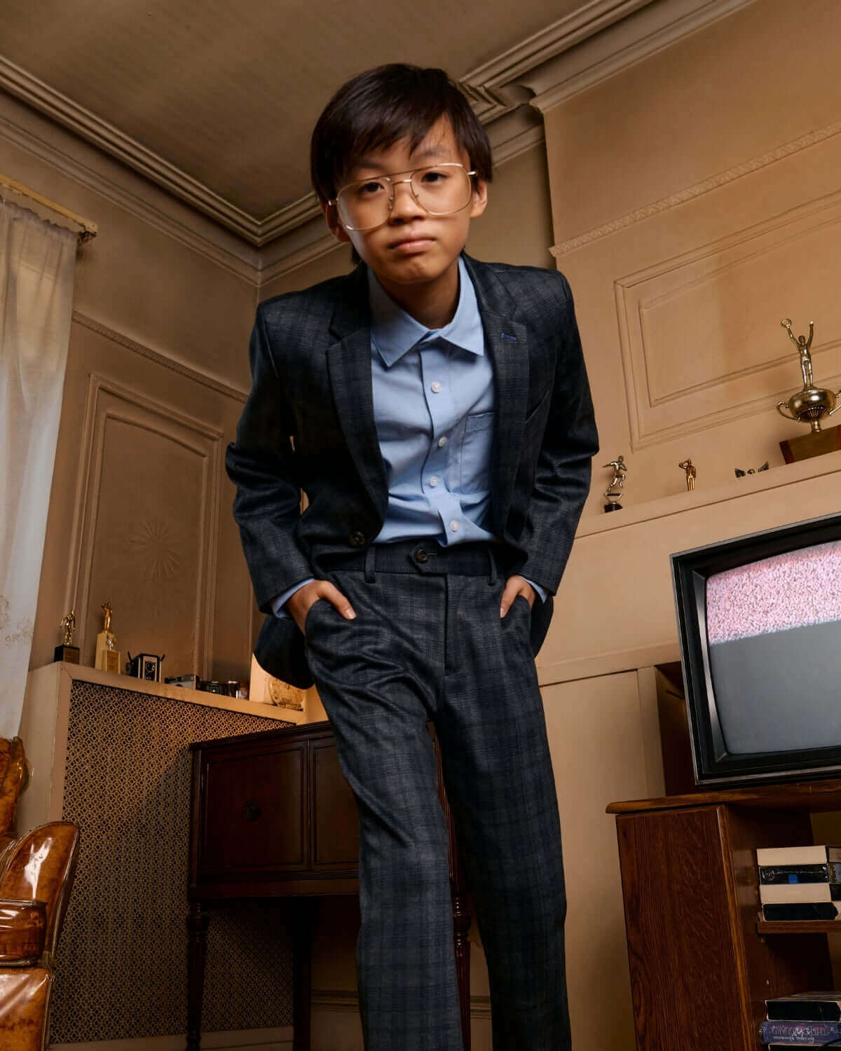 A young boy modeling the Gentleman's Plaid Stretchy Mod Suit with a stylish blue shirt and modern glasses.