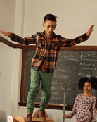 Boy balancing on a desk wearing Forest Green Highland Sweatpants and plaid shirt, showcasing cozy style in a classroom.
