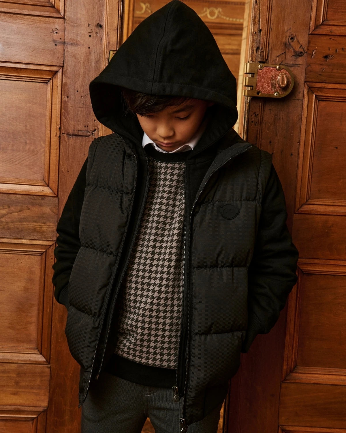 A boy walking outdoors wearing a black hooded jacket. Appaman Fall/Winter 2026 collection.