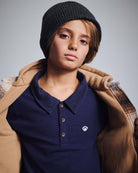 Boy wearing a Navy Blue Parker Polo with a black beanie and a tan jacket.