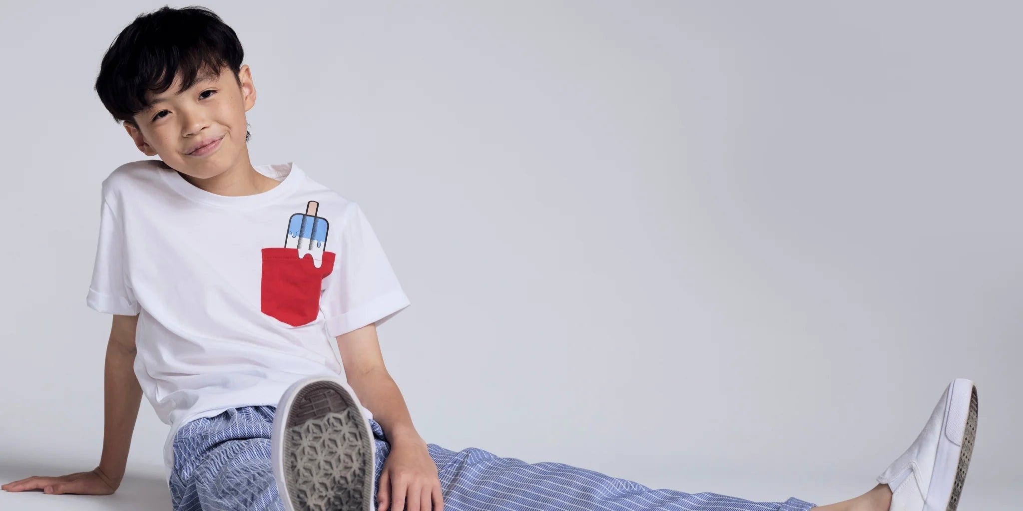 Child wearing a white t-shirt with a red and blue design, sitting on a white surface.
