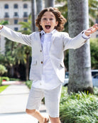 A joyful child wearing Sand Stripe Linen Trouser Shorts and a matching blazer outside, enjoying summer.