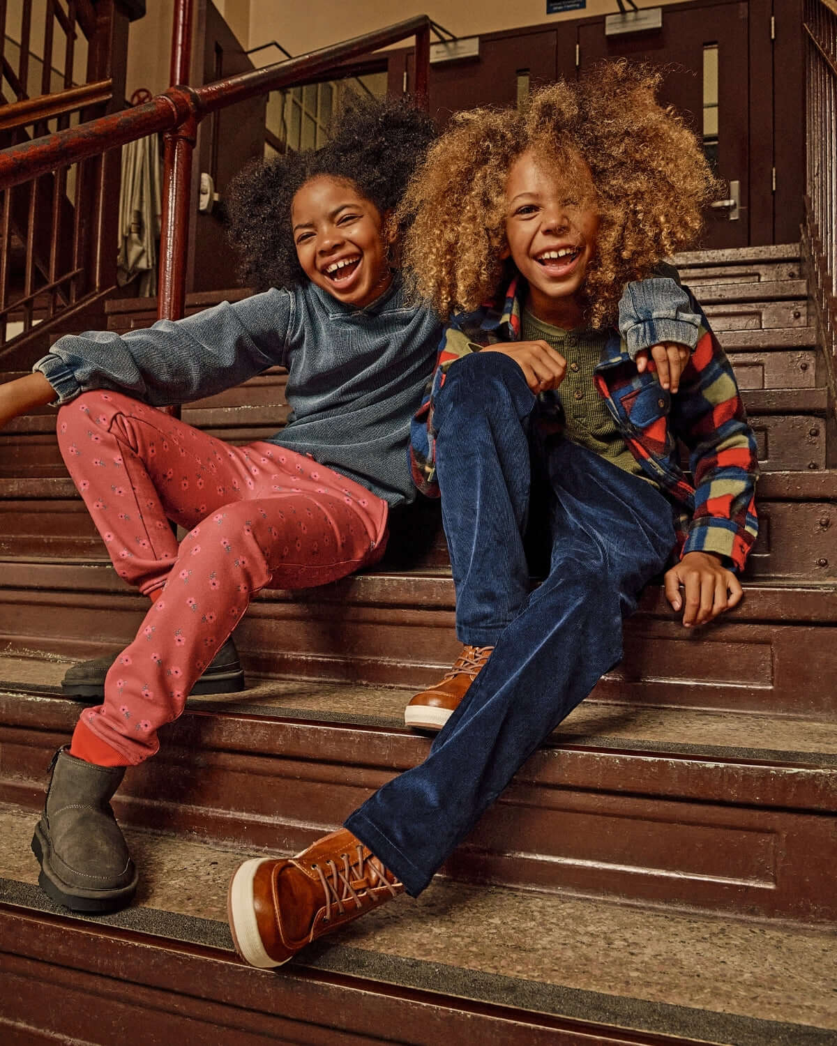 Two kids laughing on stairs wearing Cherry Blue Check Snow Fleece Shirt and stylish pants, showcasing a fun and cozy look.