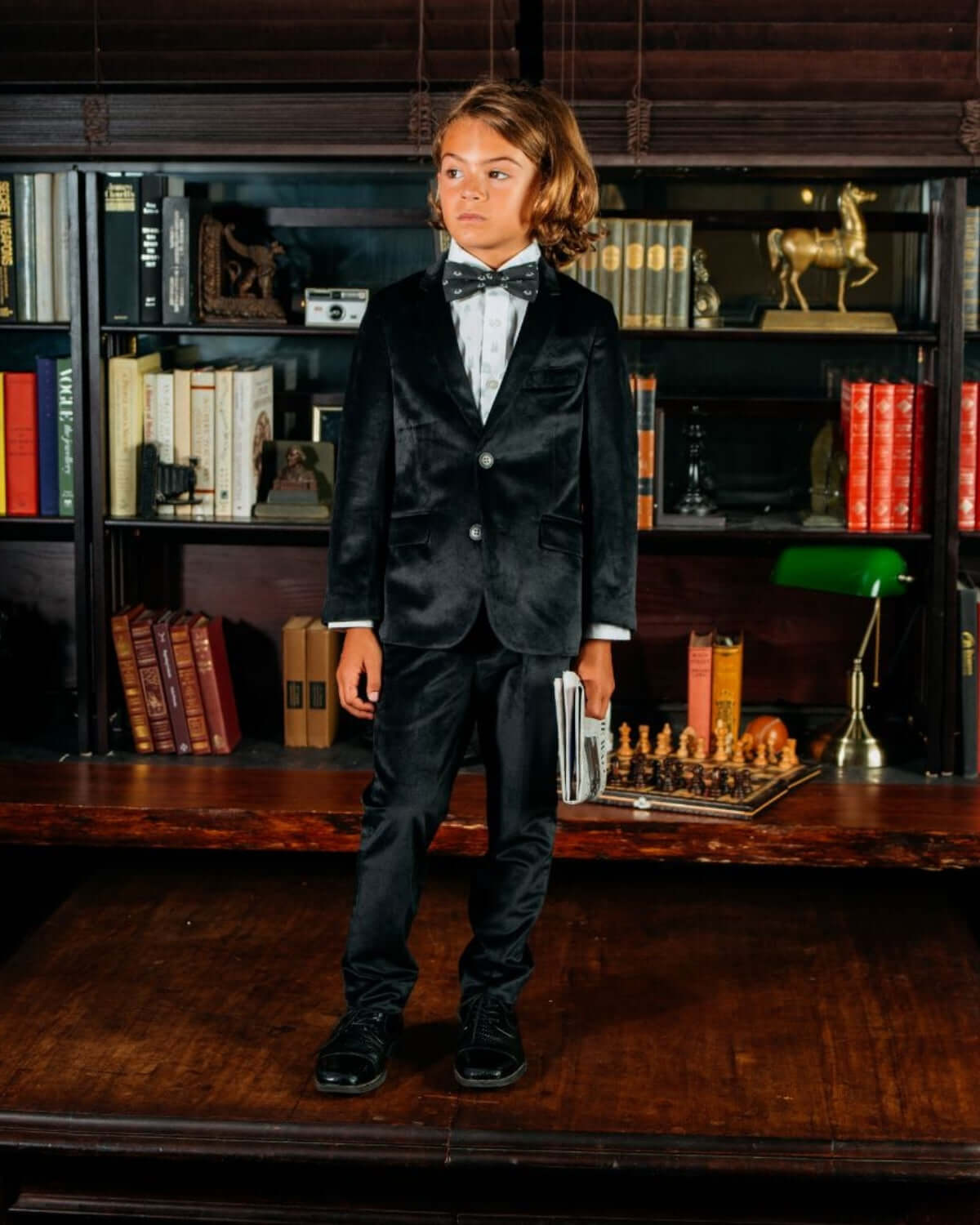A young boy wearing a black velvet suit and bow tie, representing the In The Wild Standard Button Down style.