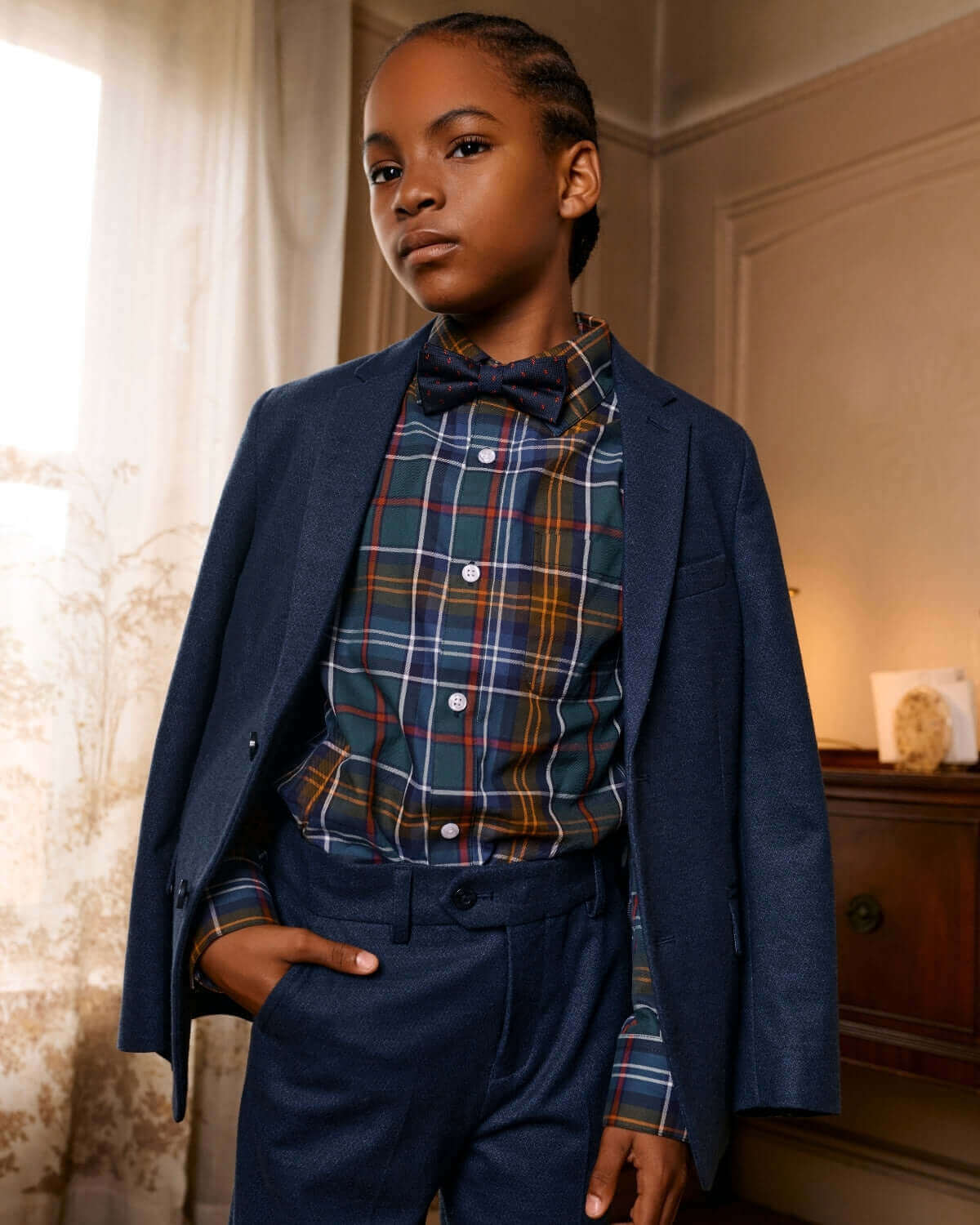 A stylish boy in a Navy Diamonds Stretchy Mod Suit with a plaid shirt and bowtie, perfect for formal occasions.
