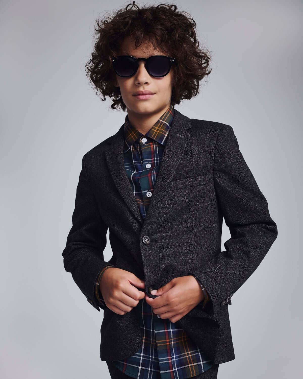 Boy wearing a Black Herringbone Stretchy Mod Suit with sunglasses and a plaid shirt.