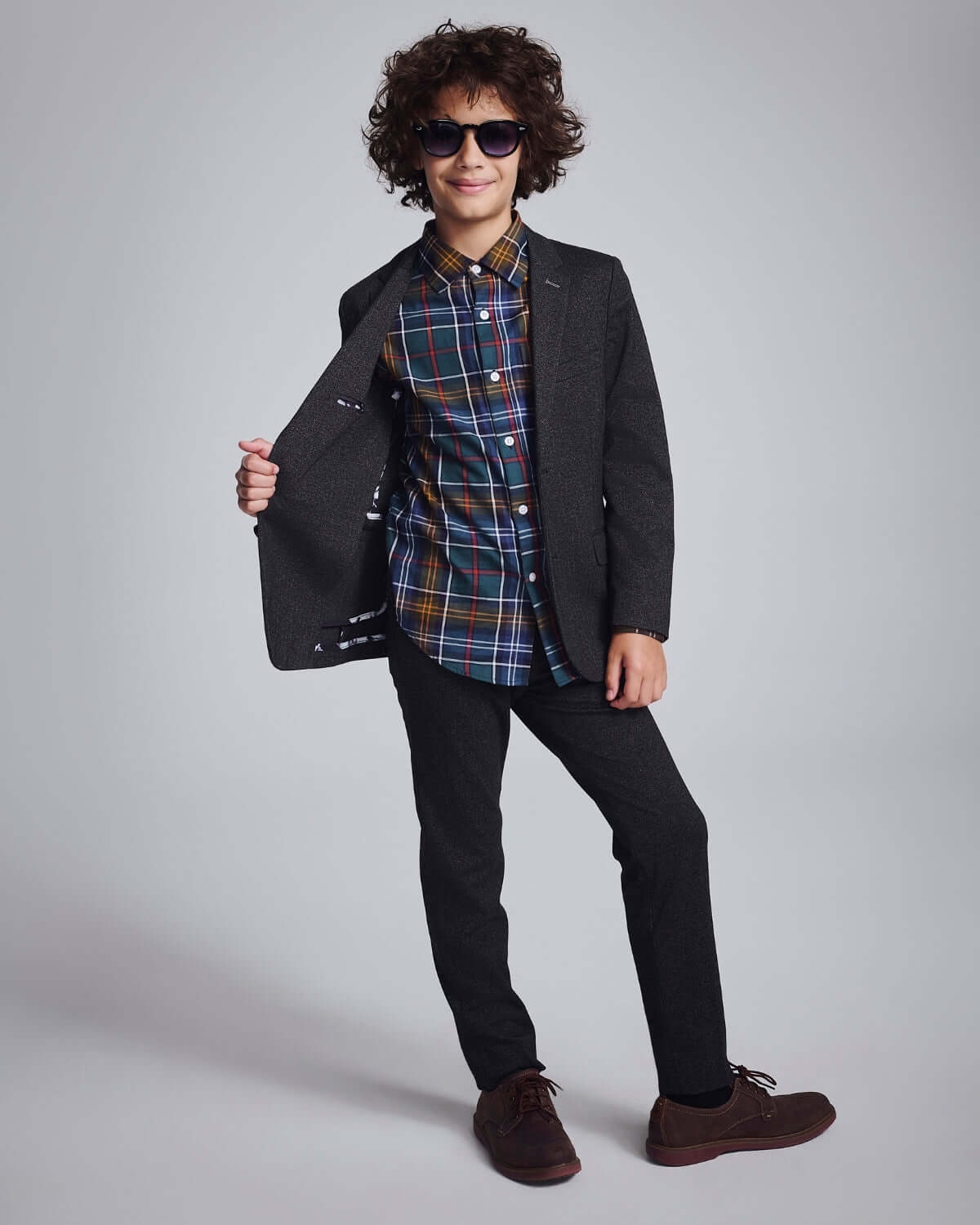 Boy wearing a Black Herringbone Stretchy Mod Suit with a colorful shirt, stylish sunglasses, and a confident pose.