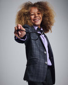 A cheerful young boy wearing a Gentleman's Plaid Stretchy Mod Suit and holding glasses, showcasing a stylish look.