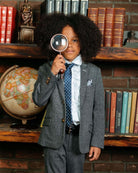 Boy wearing a Noir Micro Plaid Stretchy Mod Suit with a magnifying glass in a library setting.