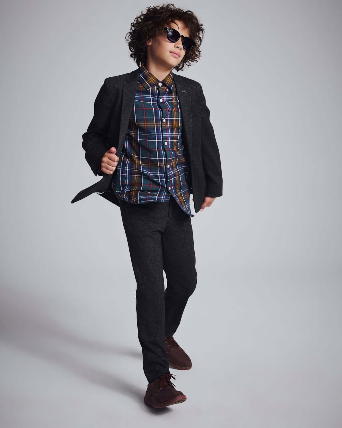 Boy confidently walking in Black Herringbone Stretchy Suit Pants and stylish sunglasses, showcasing a trendy outfit.