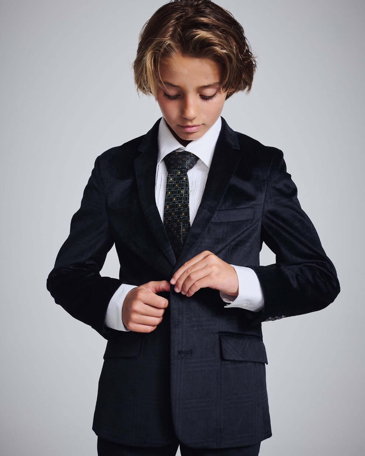 Child wearing a stylish Midnight Velvet Plaid Blazer, adjusting the jacket with a refined look.
