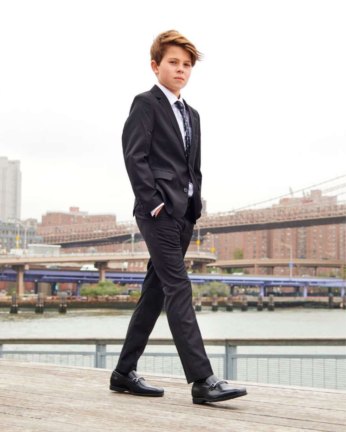 Boy wearing Black Suit Pants and a formal suit walking by the waterfront, showcasing a stylish outfit.