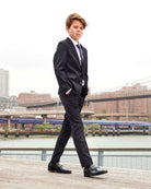 Boy wearing Black Suit Pants and a formal suit walking by the waterfront, showcasing a stylish outfit.