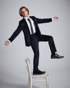 Boy modeling Midnight Velvet Plaid Suit Pants while balancing on a chair in a stylish pose.