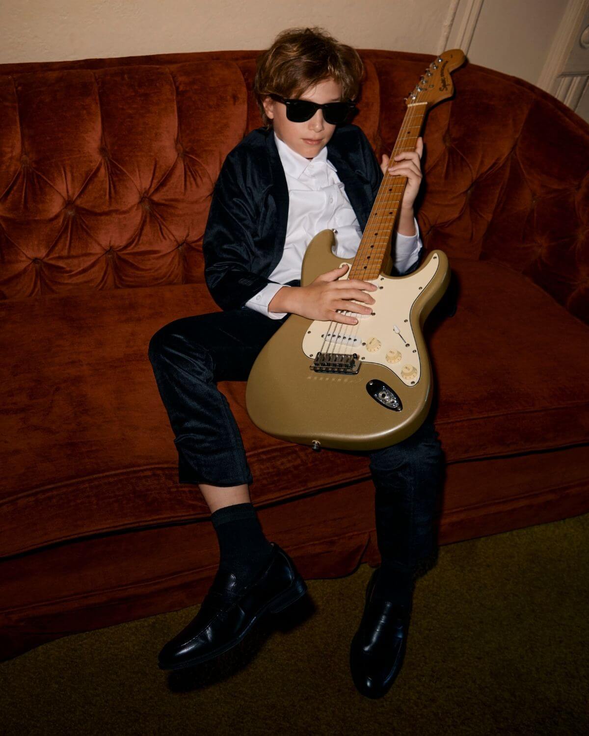 Stylish child wearing Midnight Velvet Plaid Suit Pants and sunglasses, playing a guitar on a vintage couch.