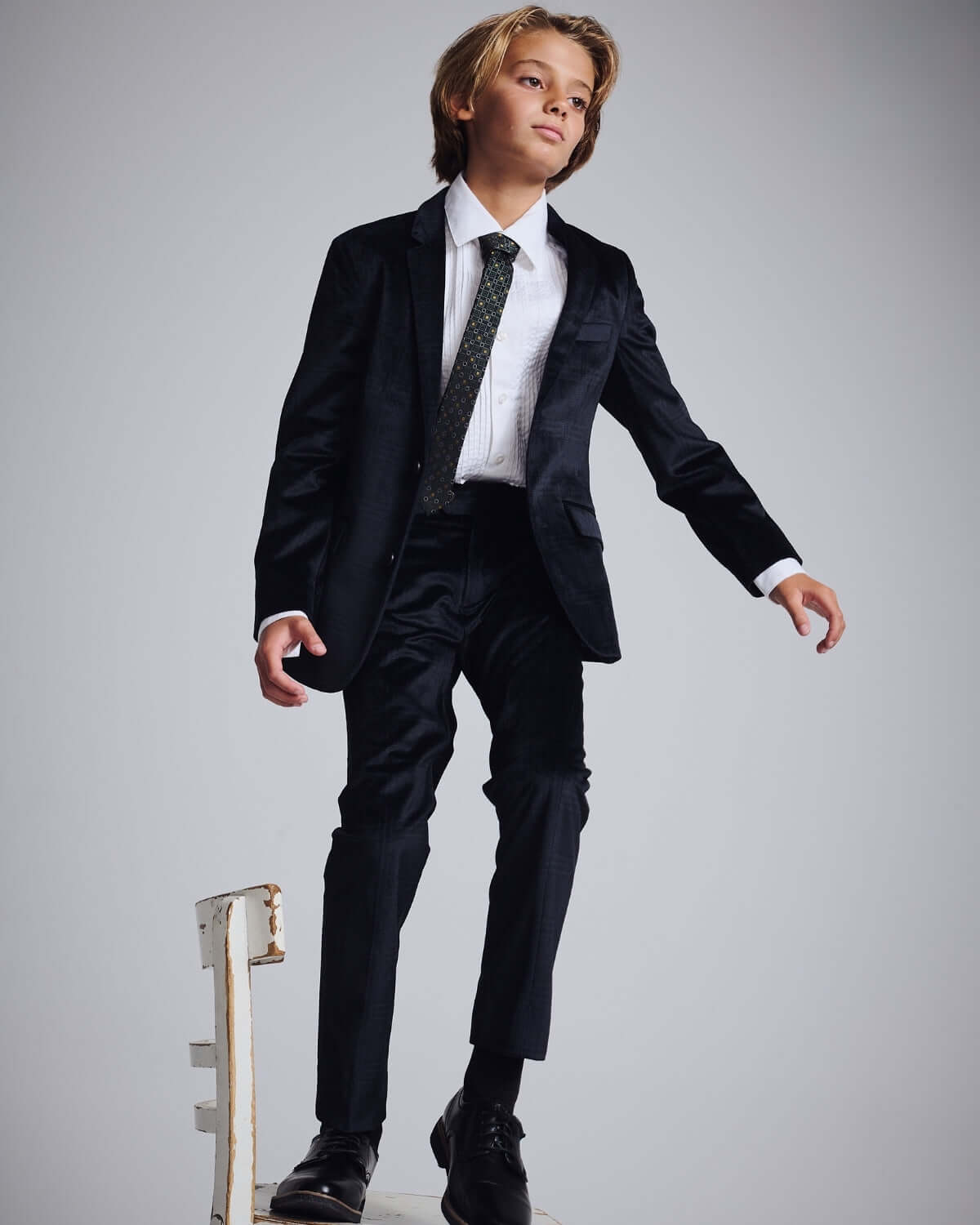 Midnight Velvet Plaid Suit Pants modeled by a boy wearing a stylish black suit and tie, showcasing luxe velvet and tailored design.