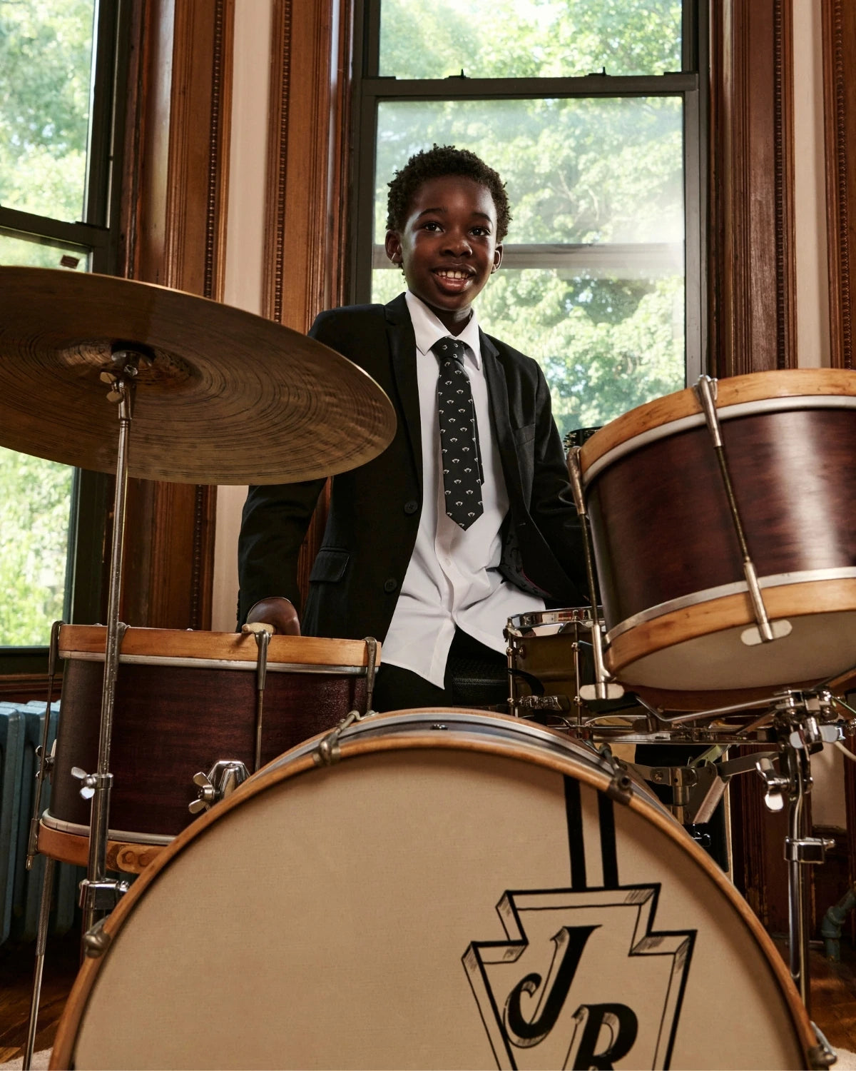 A child wearing an ivory tuxedo jacket, playing drums. Appaman Fall/Winter 2026 collection.
