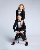 Two kids wearing Black Tuxedo Pants and bow ties, posing elegantly in a stylish formal attire.